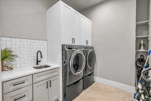 Washroom featuring light tile patterned floors, separate washer and dryer, a sink, baseboards, and cabinet space