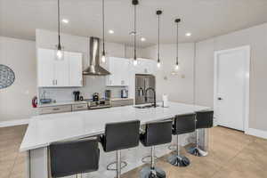 Kitchen featuring stainless steel appliances, a sink, decorative backsplash, wall chimney exhaust hood, and an island with sink