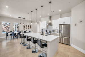 Kitchen with a sink, visible vents, wall chimney range hood, stainless steel refrigerator with ice dispenser, and backsplash