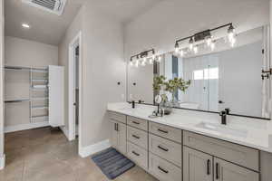 Bathroom with double vanity, baseboards, visible vents, tiled shower, and a sink