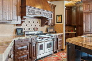 Kitchen featuring range with two ovens, decorative backsplash, wood ceiling, light stone countertops, and premium range hood