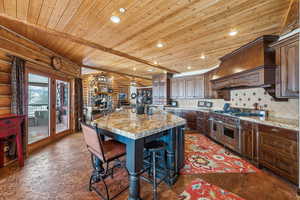 Kitchen featuring an island with sink, log walls, double oven range, backsplash, and recessed lighting