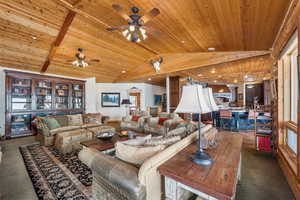 Living area featuring lofted ceiling with beams, wood ceiling, and dark colored carpet