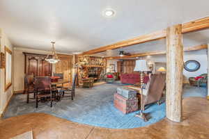 Living room featuring a textured ceiling, carpet floors, a fireplace, baseboards, and beamed ceiling