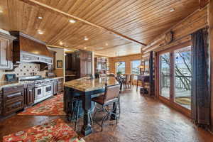 Kitchen featuring range with two ovens, a kitchen island with sink, premium range hood, a sink, and wood ceiling