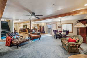 Living area with stairway, a ceiling fan, light carpet, a textured ceiling, and beamed ceiling