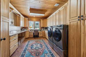 Washroom with wooden ceiling, dark tile patterned flooring, visible vents, cabinet space, and washer and clothes dryer