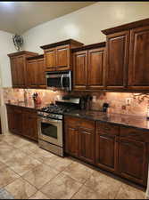 Kitchen featuring dark brown cabinets, dark stone countertops, stainless steel appliances, and decorative backsplash