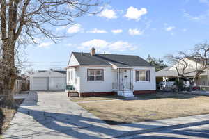 View of front of house featuring a garage, a chimney, roof with shingles, fence, and an outdoor structure