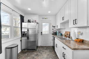 Kitchen with white cabinetry, stainless steel refrigerator with ice dispenser, and a sink