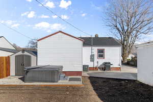 Back of property with a patio, an outdoor structure, fence, a shed, and a hot tub