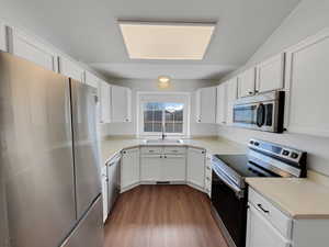 Kitchen featuring stainless steel appliances, dark wood-style flooring, white cabinets, and a sink