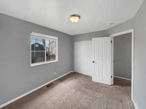 Unfurnished bedroom featuring carpet, baseboards, visible vents, and a closet