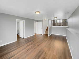 Empty room featuring wood finished floors, visible vents, baseboards, and stairs