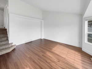 Empty room featuring vaulted ceiling, stairs, wood finished floors, and visible vents