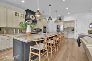 Kitchen with light stone counters, a breakfast bar area, appliances with stainless steel finishes, light wood-style floors, and a large island with sink