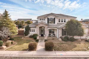 View of front of property with stucco siding, stone siding, a front lawn, and a tiled roof