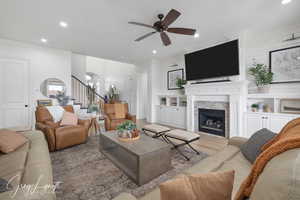 Living room featuring recessed lighting, wood finished floors, a stone fireplace, and stairs