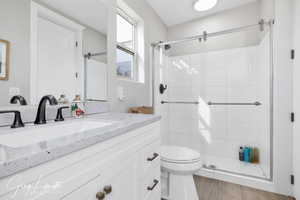 Bathroom featuring wood finished floors, a shower stall, toilet, and vanity