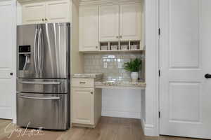 Kitchen featuring light stone counters, tasteful backsplash, light wood-style flooring, white cabinets, and stainless steel fridge with ice dispenser