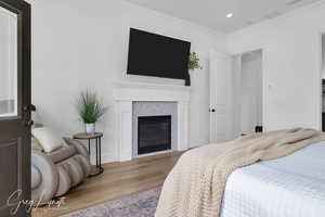 Bedroom with recessed lighting, wood finished floors, visible vents, ornamental molding, and a tiled fireplace