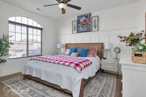 Bedroom featuring a wainscoted wall, a decorative wall, visible vents, and a ceiling fan