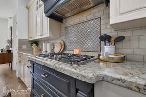 Kitchen with custom range hood, backsplash, glass insert cabinets, and stainless steel gas stovetop