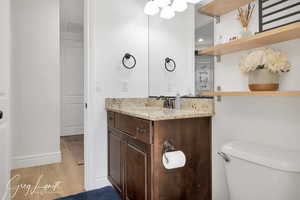 Half bathroom with toilet, wood finished floors, visible vents, vanity, and baseboards