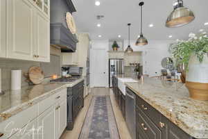 Kitchen featuring light stone counters, visible vents, appliances with stainless steel finishes, light wood-style floors, and a sink