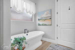 Full bath featuring a freestanding bath, wood finished floors, and baseboards