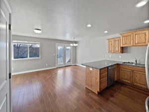 Kitchen featuring stainless steel dishwasher, dark wood-type flooring, a sink, a chandelier, and a peninsula