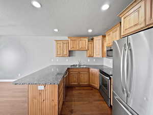 Kitchen with stainless steel appliances, dark wood-style flooring, a sink, and a peninsula