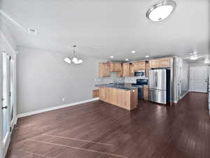 Kitchen featuring dark wood finished floors, stainless steel appliances, visible vents, a peninsula, and baseboards