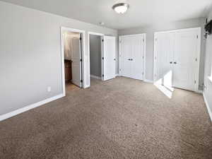 Unfurnished bedroom with carpet flooring, baseboards, and two closets