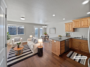 Kitchen with dark countertops, dark wood-type flooring, a peninsula, stainless steel dishwasher, and a sink