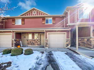 Townhome / multi-family property with a porch, stone siding, and a garage