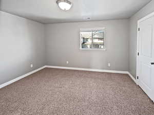 Spare room featuring a textured ceiling, carpet, visible vents, and baseboards