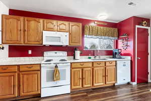 Kitchen featuring white appliances, visible vents, brown cabinets, dark wood-style flooring, and a sink