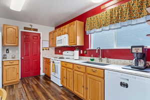 Kitchen with white appliances, dark wood-style floors, and a sink