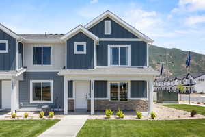 View of front of property featuring board and batten siding, stone siding, roof with shingles, and a front lawn