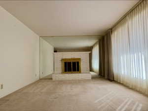 Unfurnished living room featuring light carpet and a brick fireplace