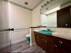 Bathroom with a skylight, visible vents, toilet, vanity, and wood finished floors