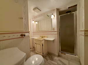 Bathroom with a textured ceiling, toilet, a shower stall, and wallpapered walls