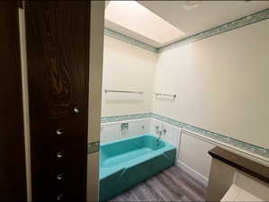 Full bath featuring a skylight, wood finished floors, and a bath