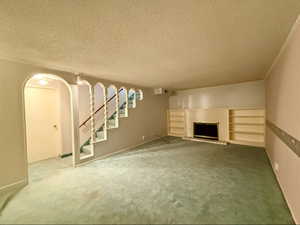 Living room area featuring arched walkways, a textured ceiling, a fireplace, carpet flooring, and stairway