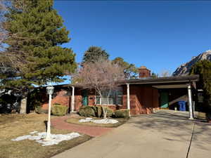 View of front of house with an attached carport, brick siding, driveway, and a chimney