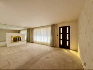 Living room with carpet, a brick fireplace, and wallpapered walls and front door