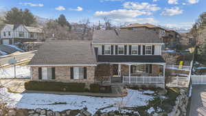 View of front of home featuring brick siding, a shingled roof, covered porch, fence, and a residential view