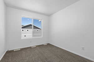 Unfurnished room with a textured ceiling, dark colored carpet, visible vents, and baseboards