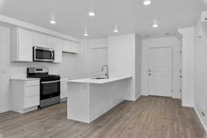 Kitchen with appliances with stainless steel finishes, white cabinetry, a sink, and light wood-style flooring